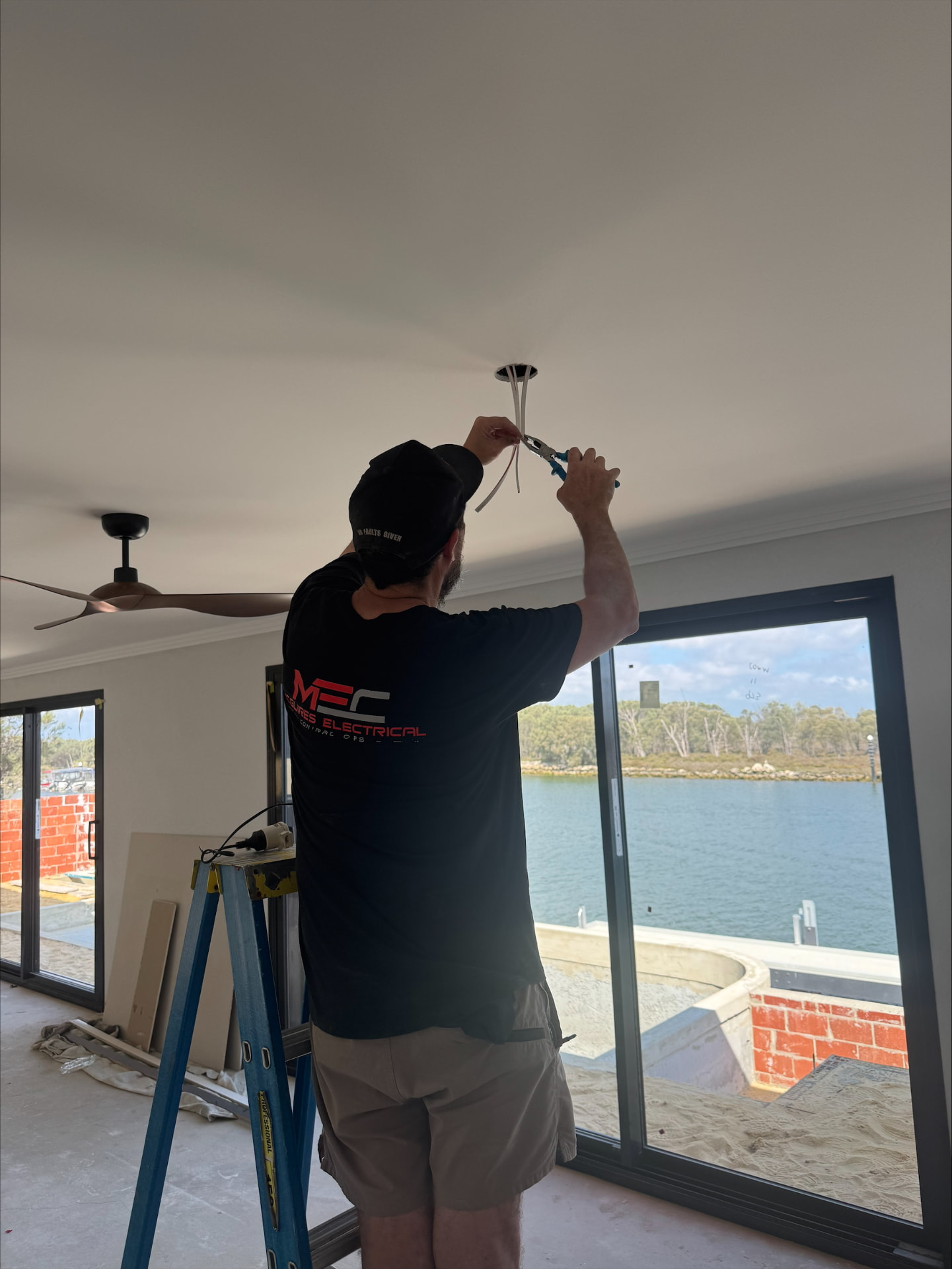 McGuires Electrical contractor in MEC-branded shirt wiring a recessed downlight point in a Perth home ceiling