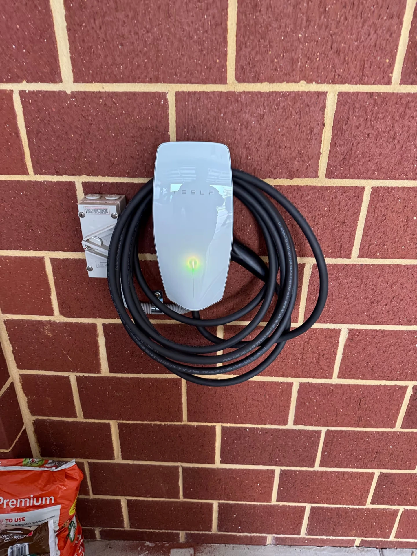 Tesla Wall Connector EV charger mounted on a brick wall by McGuires Electrical