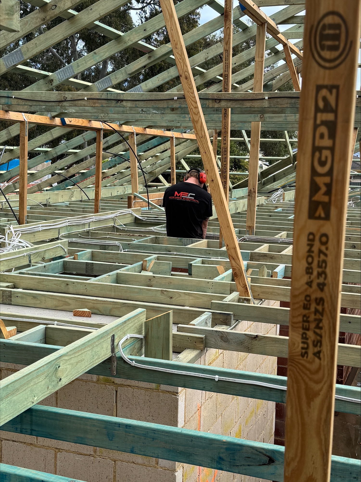 McGuires Electrical electrician roughing in cabling through the timber roof framing of a new home at Glen Iris, Jandakot