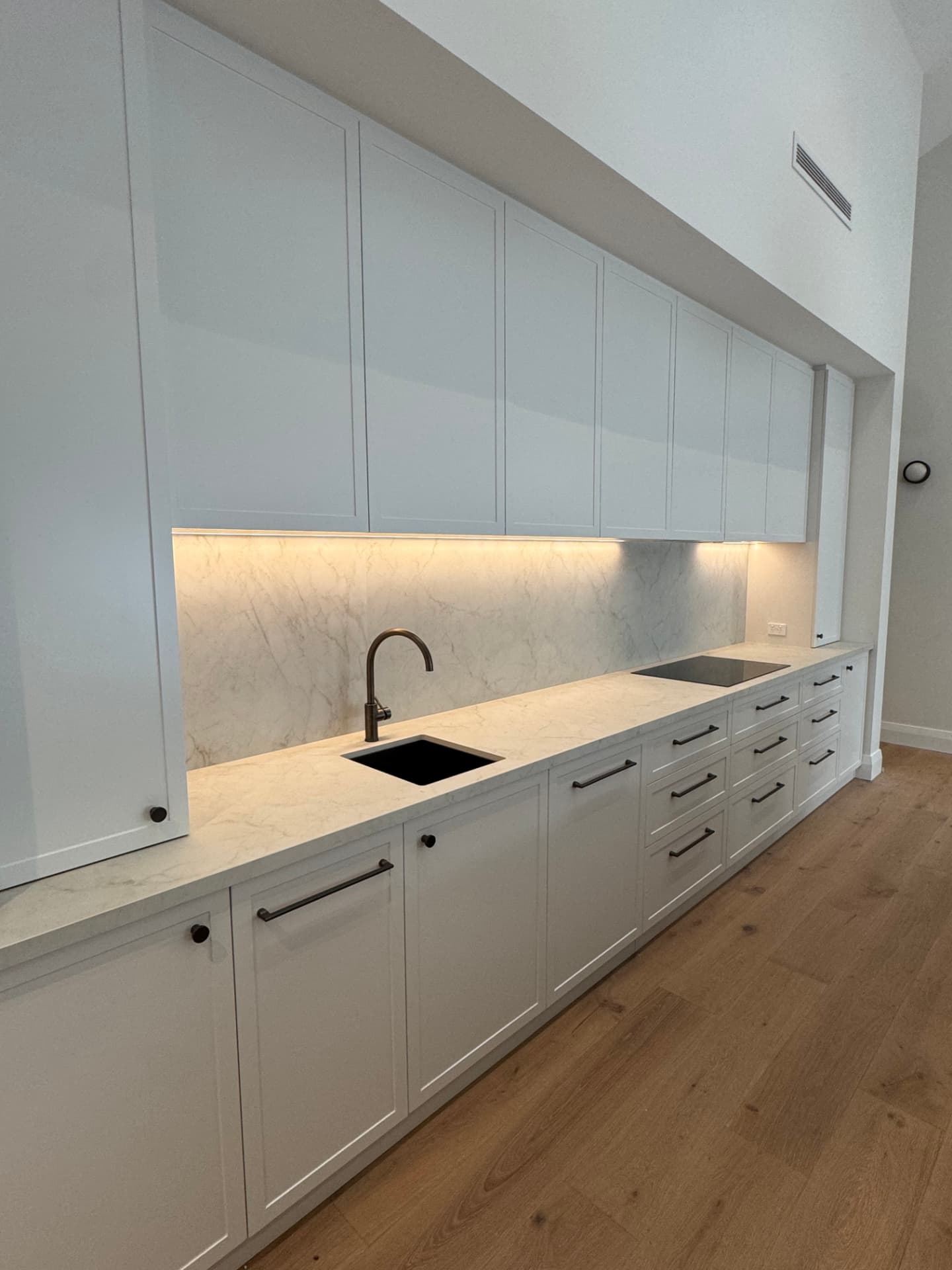 Renovated kitchen in Nedlands with white shaker cabinetry, marble-look splashback and warm under-cabinet LED lighting installed by McGuires Electrical