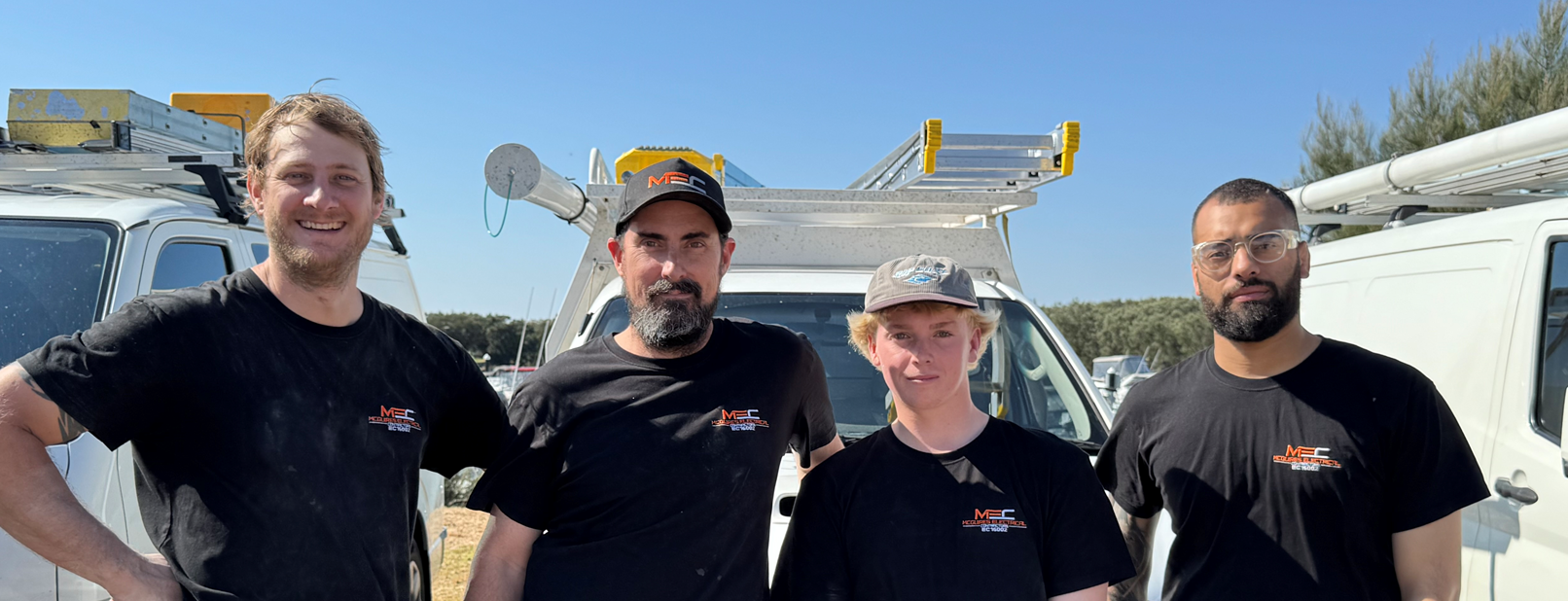 The McGuires Electrical Contractors team of four licensed electricians in branded shirts in front of their white service vans in Perth's southern suburbs